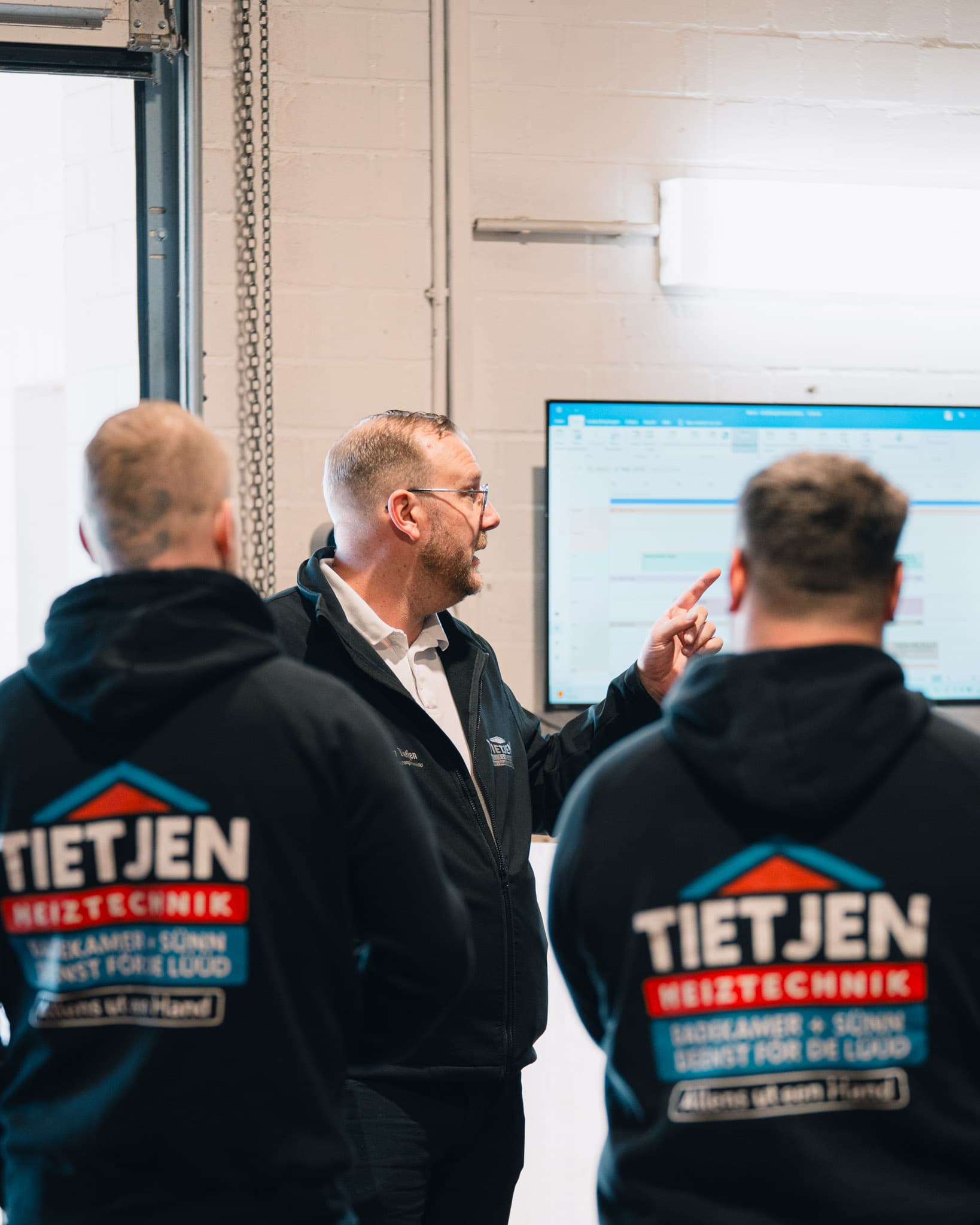 Benjamin Tietjen erklärt zwei Mitarbeitern am Bildschirm die Tourenplanung